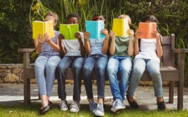 students sitting on a bench, reading, with faces mostly covered by their books.
